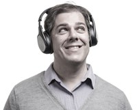 Photo en noir et blanc de Frank Russo, vêtu d’une chemise à col et d’un cardigan, portant un casque audio sans fil, souriant et levant les yeux vers sa gauche, sur fond blanc.