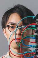 A headshot of Taichi Kumon with an analogue sythesizer visible on the right border with coloured cables connected and crossing across their face