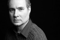 Gilles Gobeil in a black and white headshot photo wearing a wool sweater over a dark long collared shirt, against a black background. 