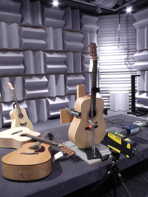 Des guitares posées sur une plate-forme dans un laboratoire, avec du matériel de mesure disposé un peu partout dans la pièce.